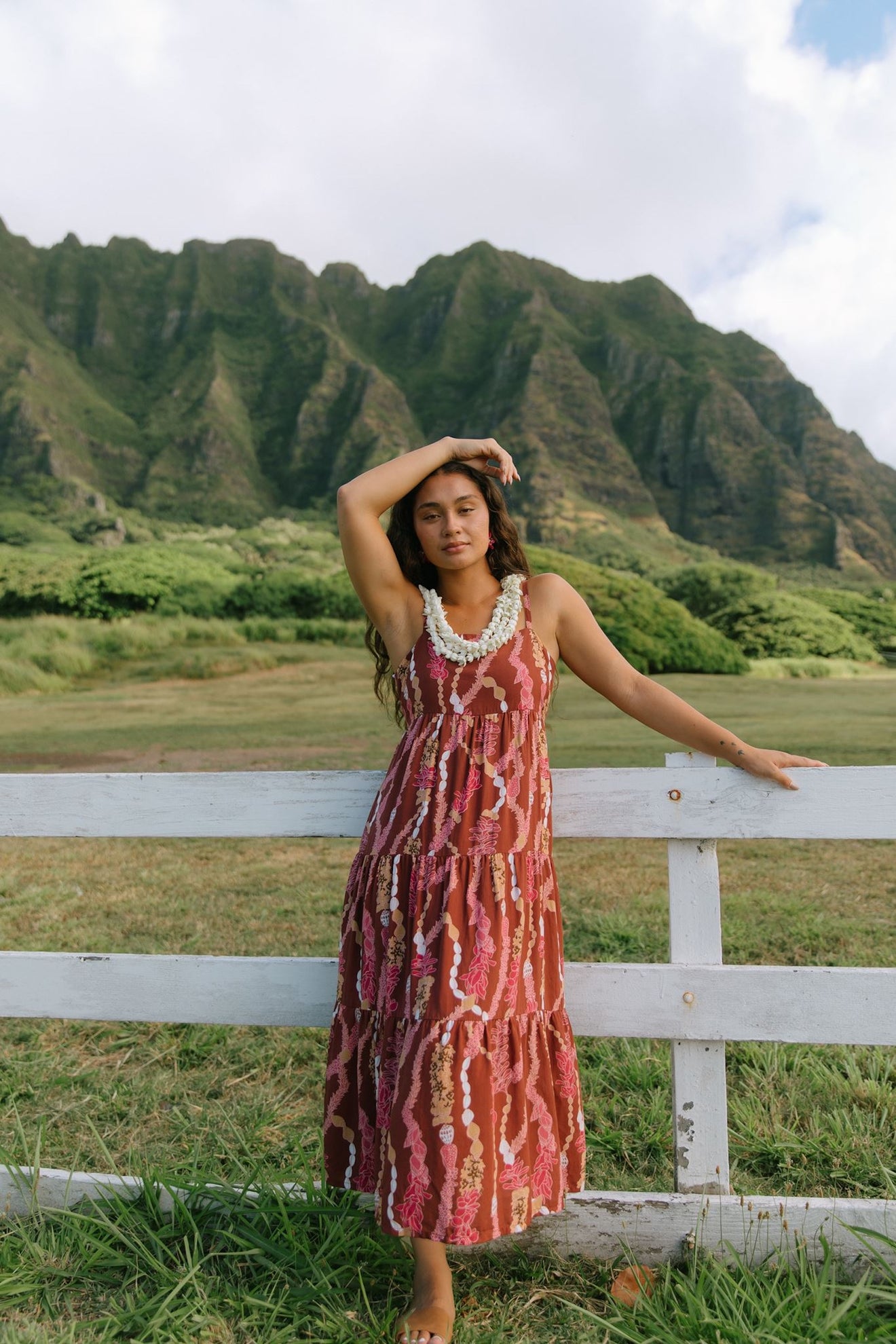 woman with brown hair wearing red-brown maxi dress with lei print