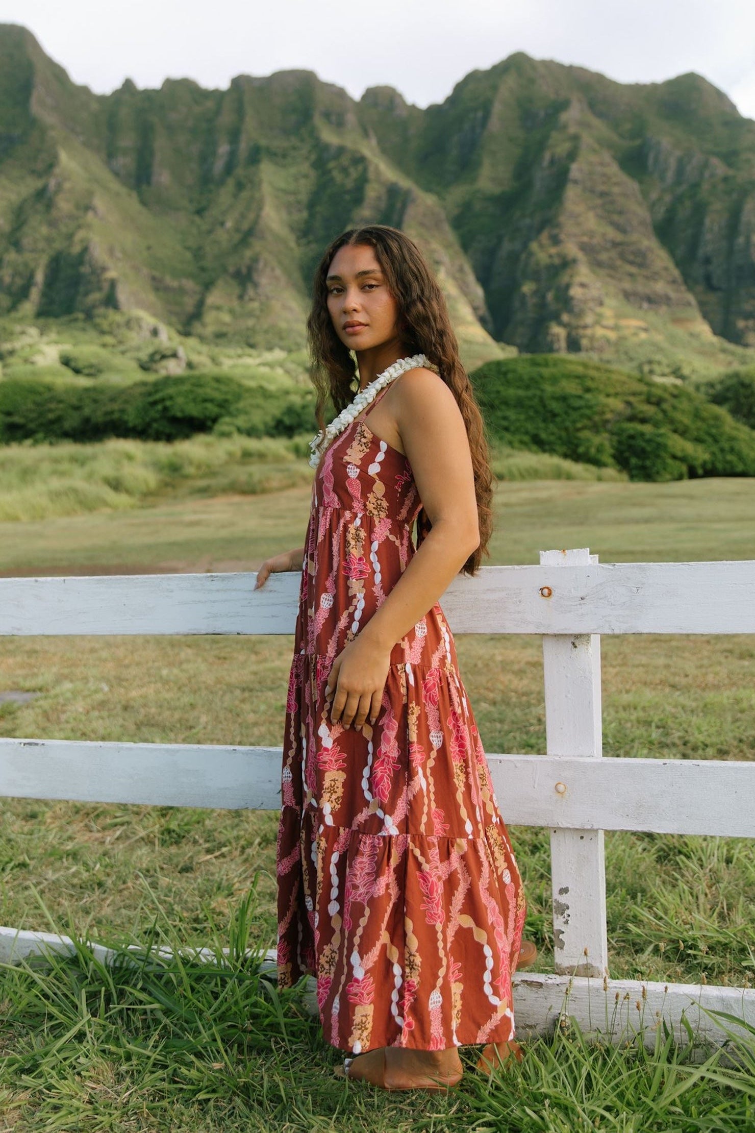woman with brown hair wearing red-brown maxi dress with lei print