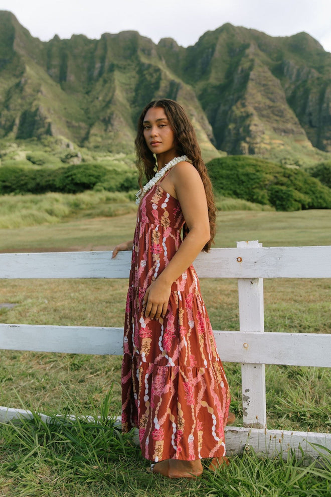 woman with brown hair wearing red-brown maxi dress with lei print