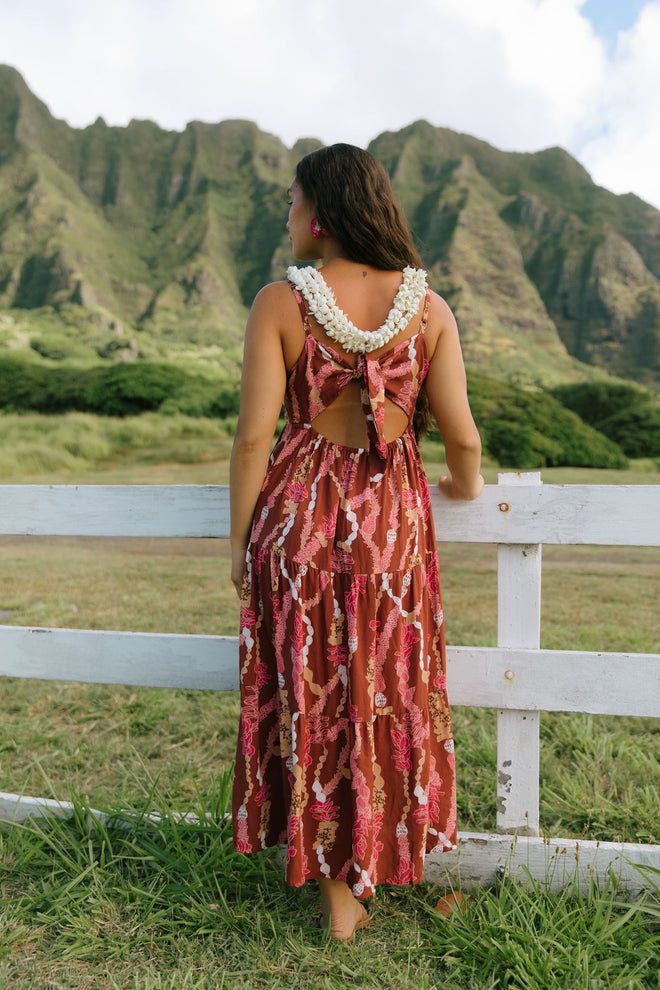 woman with brown hair wearing red-brown maxi dress with lei print