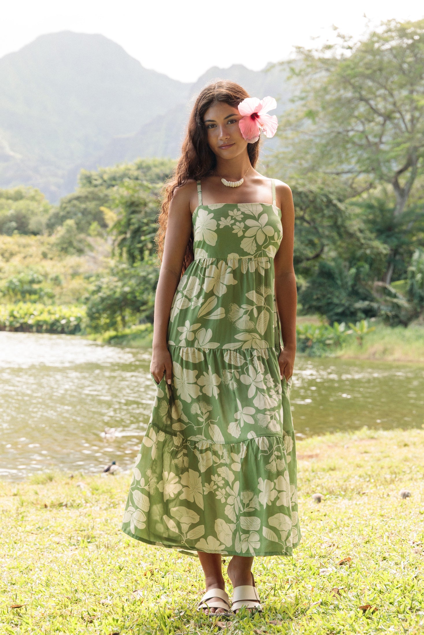 woman with brown hair wearing green tie back dress with nativr hawaiian plants