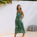 woman with brown hair wearing lush green maxi spaghetti strap dress with a tie back detail and puakenikeni print