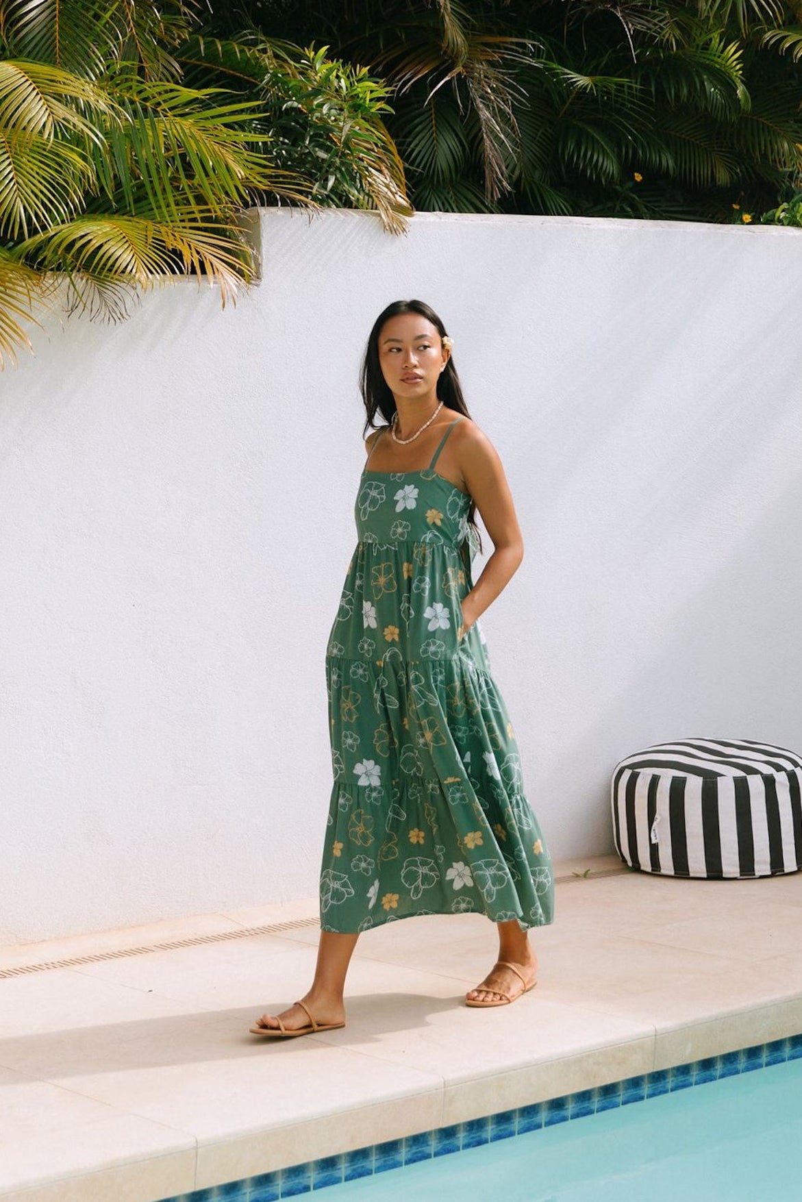 woman with brown hair wearing lush green maxi spaghetti strap dress with a tie back detail and puakenikeni print