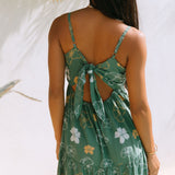 woman with brown hair wearing lush green maxi spaghetti strap dress with a tie back detail and puakenikeni print