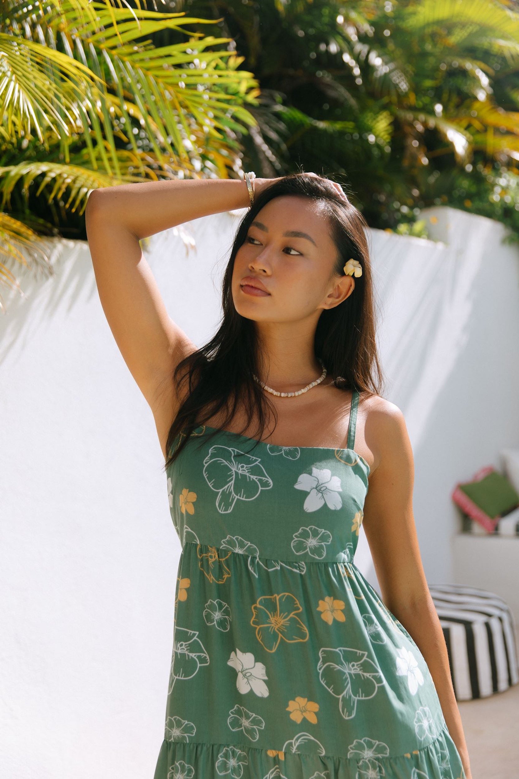 woman with brown hair wearing lush green maxi spaghetti strap dress with a tie back detail and puakenikeni print