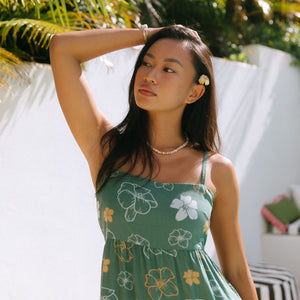 woman with brown hair wearing lush green maxi spaghetti strap dress with a tie back detail and puakenikeni print