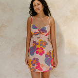 Woman in short tank dress with multi colored floral on light pink ground.