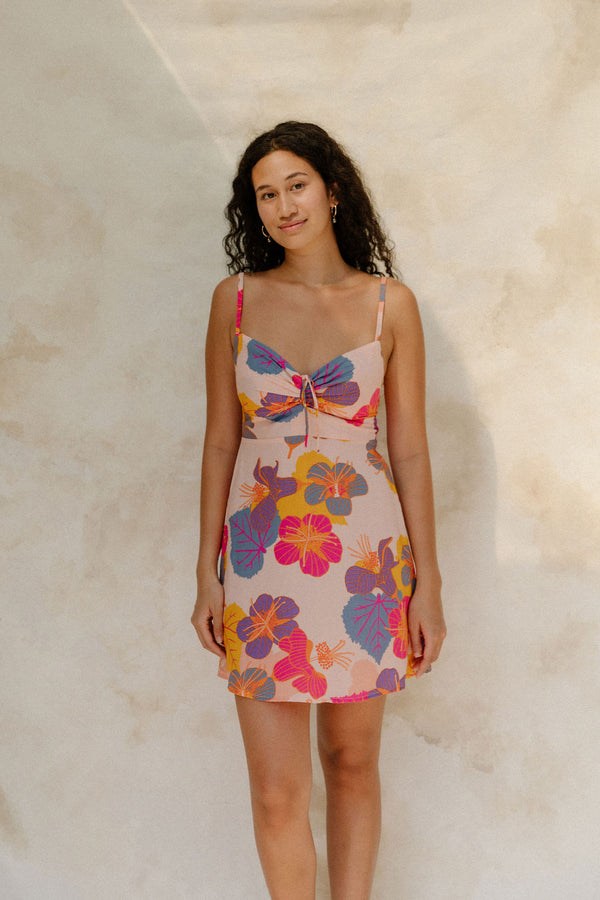 Woman in short tank dress with multi colored floral on light pink ground.