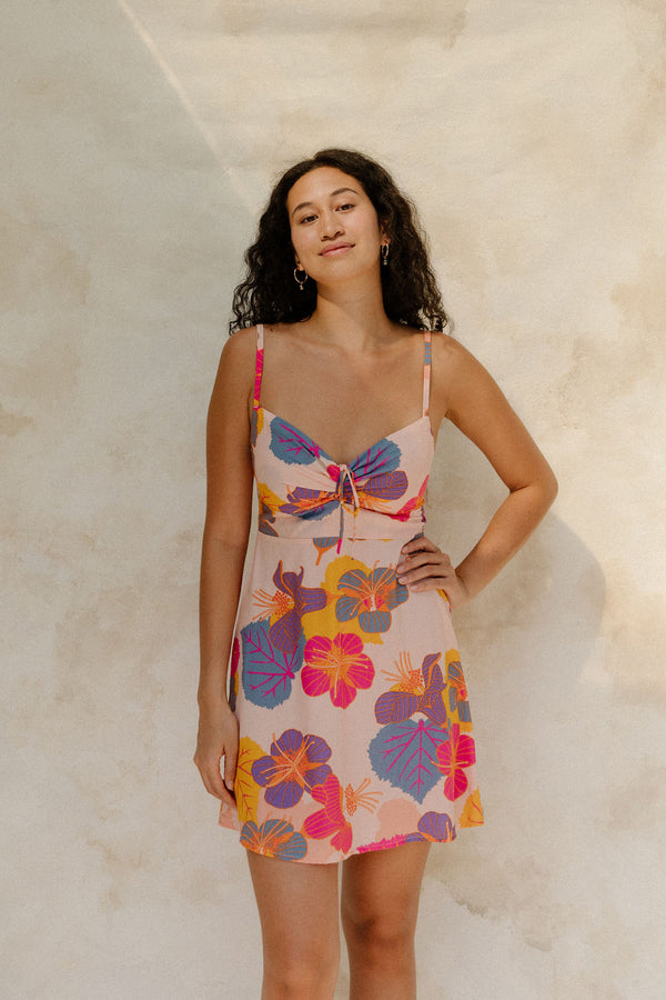 Woman in short tank dress with multi colored floral on light pink ground.