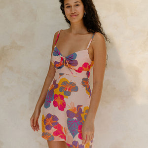 Woman in short tank dress with multi colored floral on light pink ground.