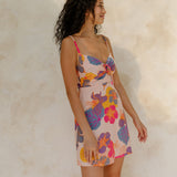Woman in short tank dress with multi colored floral on light pink ground.
