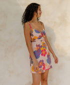 Woman in short tank dress with multi colored floral on light pink ground.