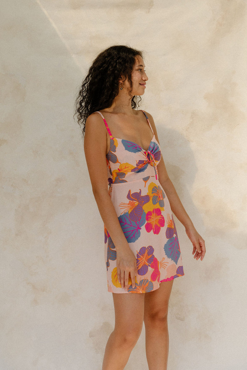 Woman in short tank dress with multi colored floral on light pink ground.