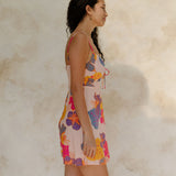 Woman in short tank dress with multi colored floral on light pink ground.