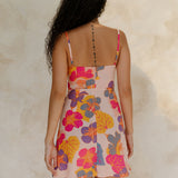 Woman in short tank dress with multi colored floral on light pink ground.