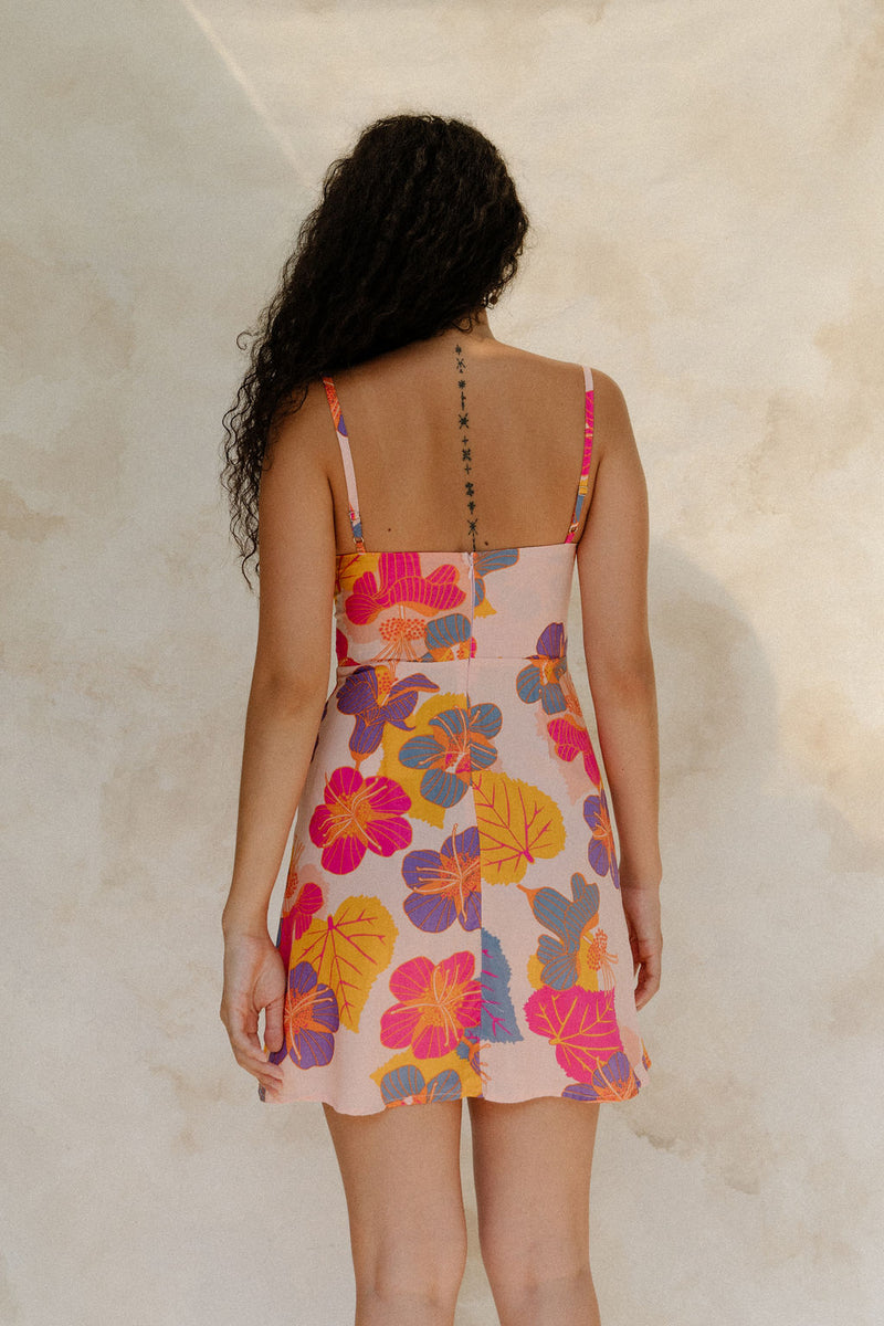 Woman in short tank dress with multi colored floral on light pink ground.