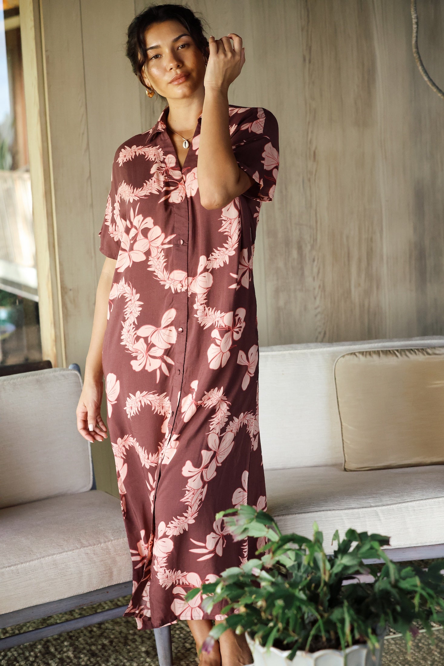 woman with brown hair wearing a brown colored maxi button up dress with light pink lei awapuhi print