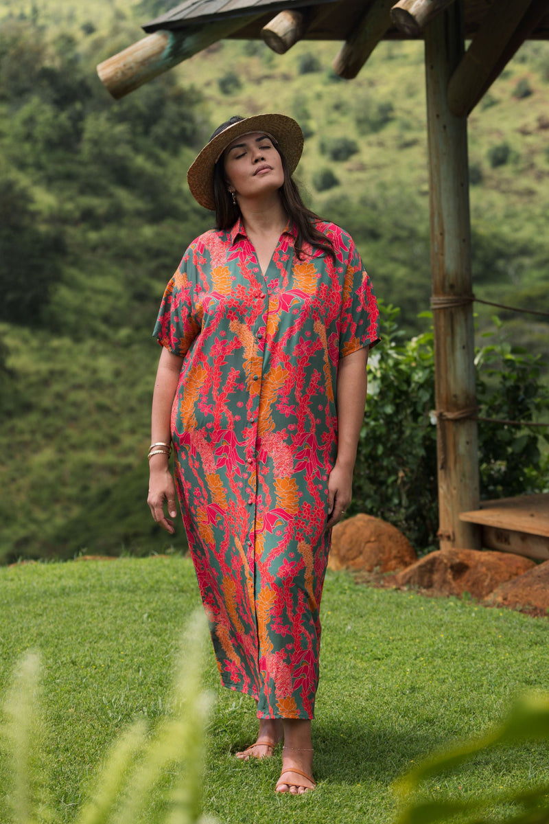 woman with brown hair wearing a colorful maxi button up dress with tropical lei print