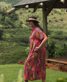woman with brown hair wearing a colorful maxi button up dress with tropical lei print
