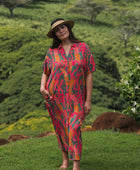 woman with brown hair wearing a colorful maxi button up dress with tropical lei print