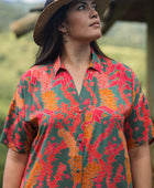 woman with brown hair wearing a colorful maxi button up dress with tropical lei print