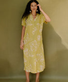 Woman in long short sleeve shirt dress with beige floral print on light green ground.