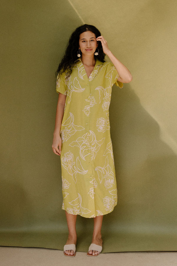 Woman in long short sleeve shirt dress with beige floral print on light green ground.