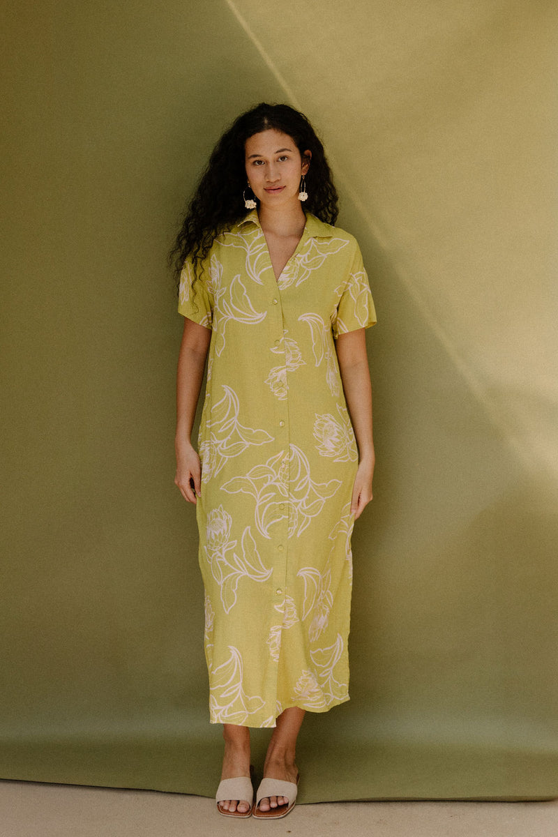 Woman in long short sleeve shirt dress with beige floral print on light green ground.