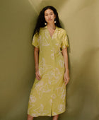 Woman in long short sleeve shirt dress with beige floral print on light green ground.