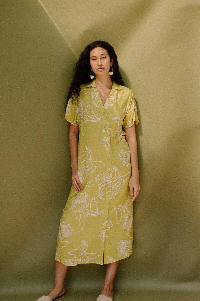 Woman in long short sleeve shirt dress with beige floral print on light green ground.