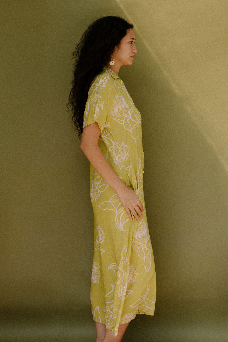 Woman in long short sleeve shirt dress with beige floral print on light green ground.