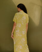 Woman in long short sleeve shirt dress with beige floral print on light green ground.