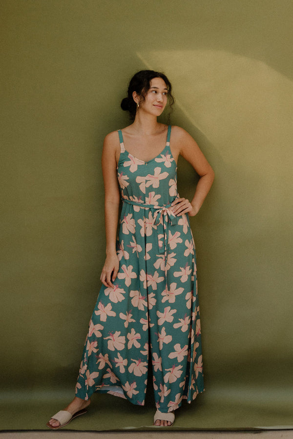 Woman wearing long sleeveless jumpsuit with light pink floral print on green ground.