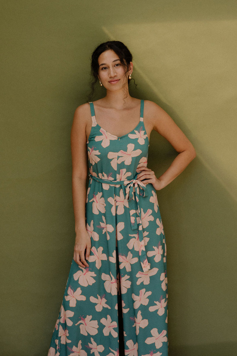 Woman wearing long sleeveless jumpsuit with light pink floral print on green ground.