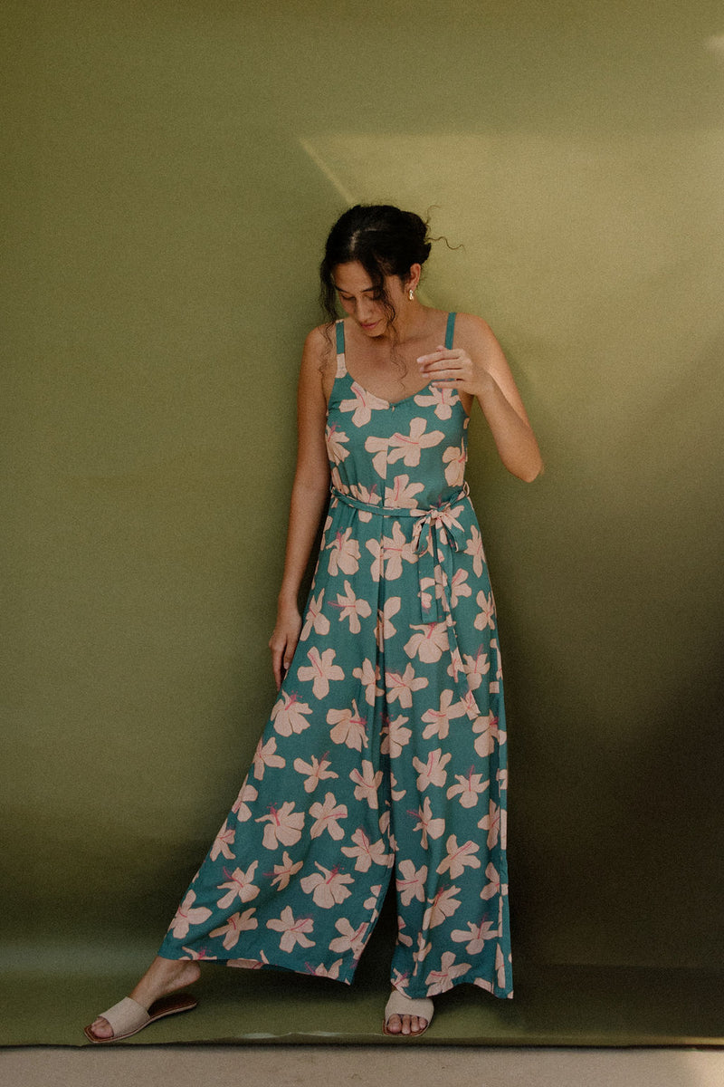 Woman wearing long sleeveless jumpsuit with light pink floral print on green ground.