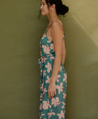 Woman wearing long sleeveless jumpsuit with light pink floral print on green ground.