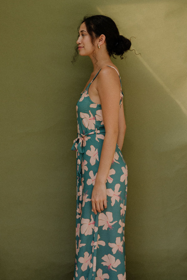 Woman wearing long sleeveless jumpsuit with light pink floral print on green ground.