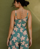 Woman wearing long sleeveless jumpsuit with light pink floral print on green ground.