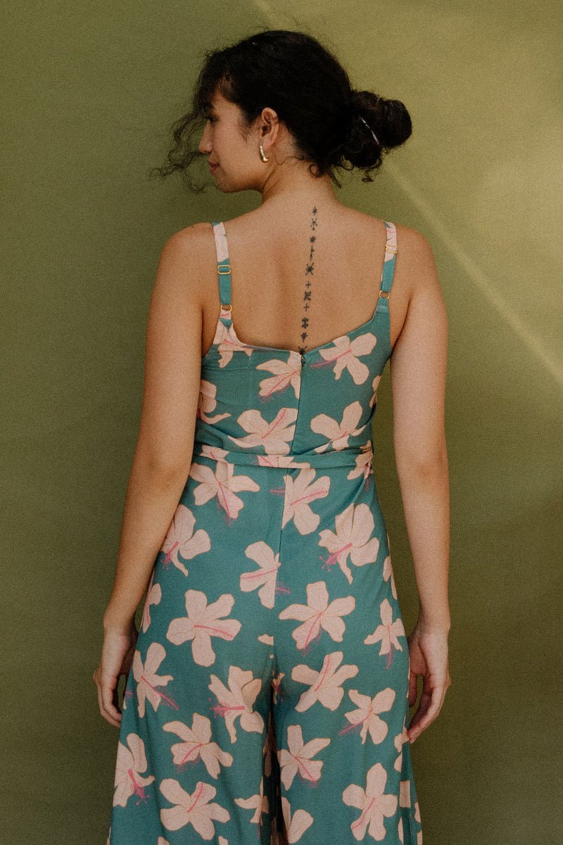 Woman wearing long sleeveless jumpsuit with light pink floral print on green ground.