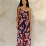 Woman in long sleeveless jumpsuit with print floral print on dark navy ground.