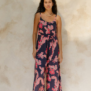 Woman in long sleeveless jumpsuit with print floral print on dark navy ground.