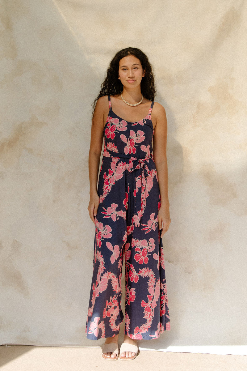 Woman in long sleeveless jumpsuit with print floral print on dark navy ground.