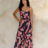 Woman in long sleeveless jumpsuit with print floral print on dark navy ground.