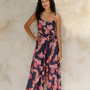 Woman in long sleeveless jumpsuit with print floral print on dark navy ground.