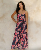 Woman in long sleeveless jumpsuit with print floral print on dark navy ground.