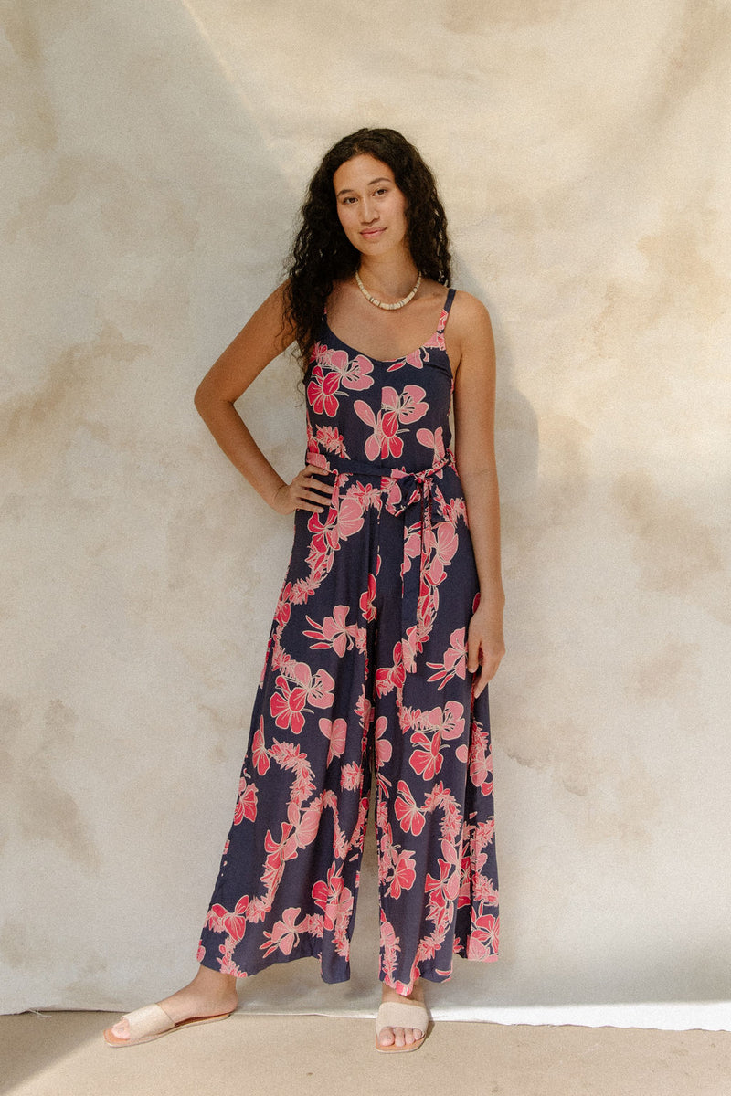 Woman in long sleeveless jumpsuit with print floral print on dark navy ground.