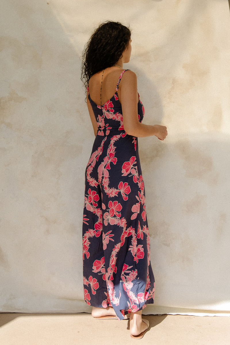 Woman in long sleeveless jumpsuit with print floral print on dark navy ground.