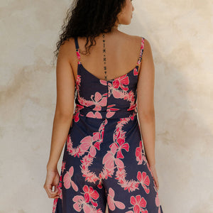 Woman in long sleeveless jumpsuit with print floral print on dark navy ground.