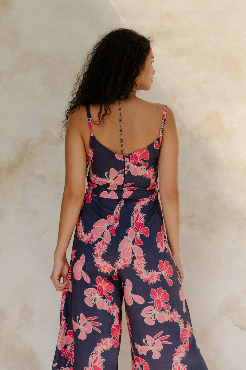 Woman in long sleeveless jumpsuit with print floral print on dark navy ground.