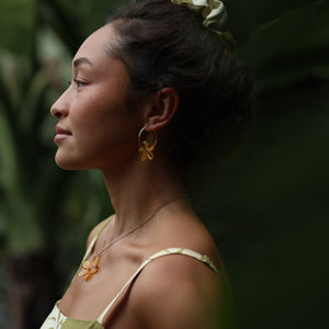 woman with brown hair wearing yellow glass plumeria necklace and earrings 